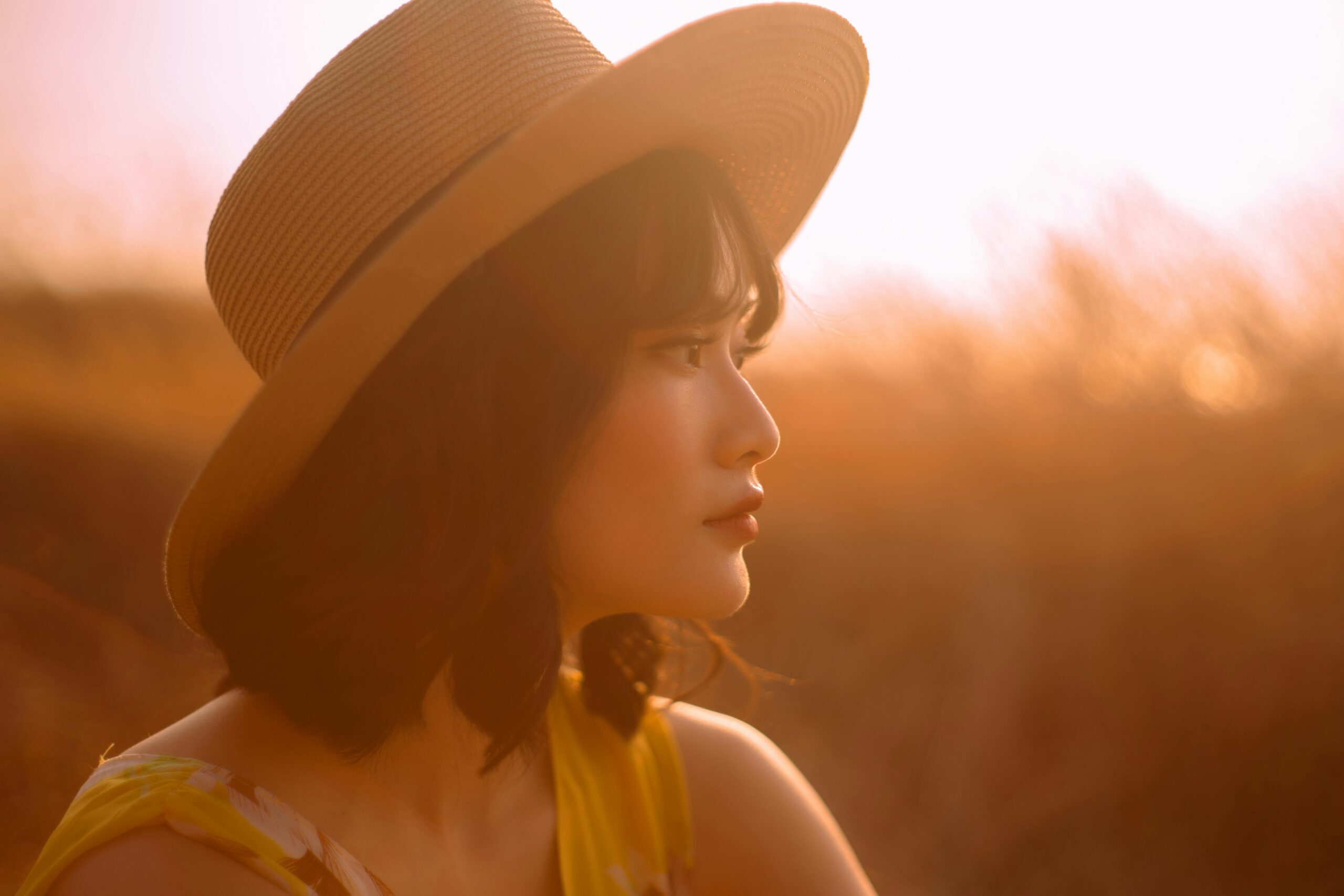 A serene side profile of a woman in a straw hat, captured at sunset for a warm, dreamy mood.